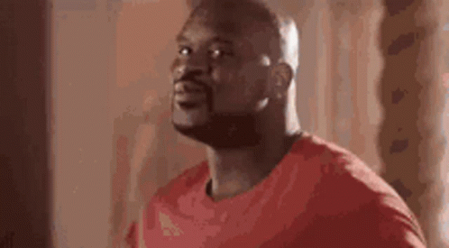 A Man In A Red Shirt Is Standing In Front Of A Window And Looking Up . GIF