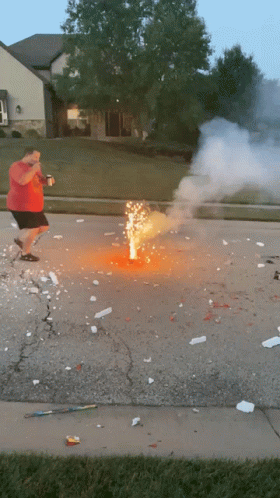 A Man In A Red Shirt Is Standing Next To A Firework Display GIF