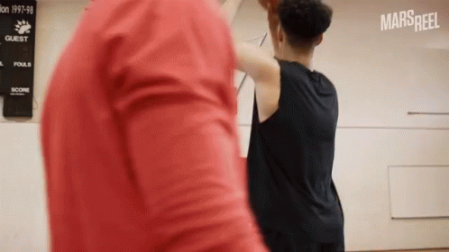 A Man In A Red Shirt Is Standing Next To A Man In A Black Shirt Playing Basketball .. GIF
