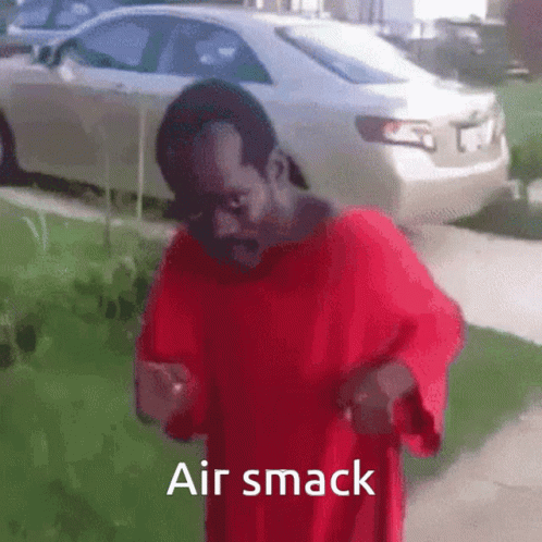A Man In A Red Shirt Is Standing On A Sidewalk With The Words Air Smack Above Him . GIF
