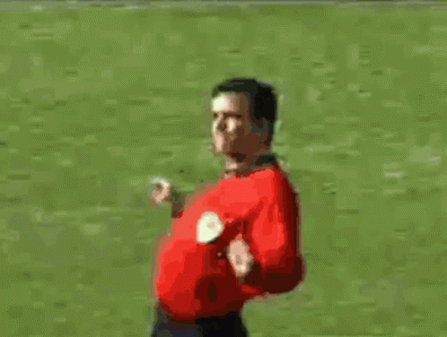 A Man In A Red Shirt Is Standing On A Soccer Field With His Arms Outstretched GIF
