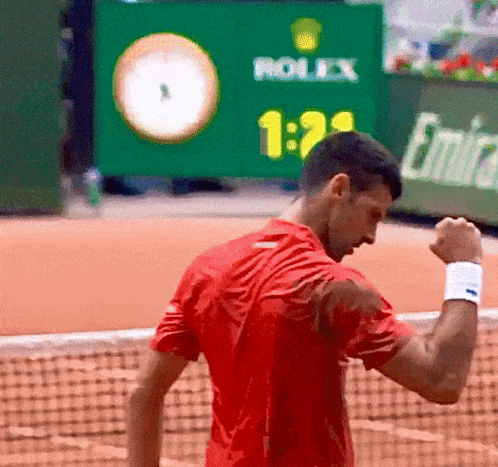 A Man In A Red Shirt Is Standing On A Tennis Court With A Rolex Sign In The Background GIF
