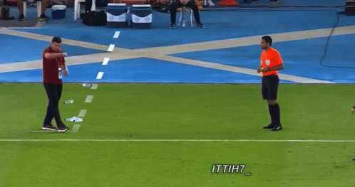 A Man In A Red Shirt Is Talking To A Referee On A Soccer Field With Ittih7 Written On The Bottom GIF