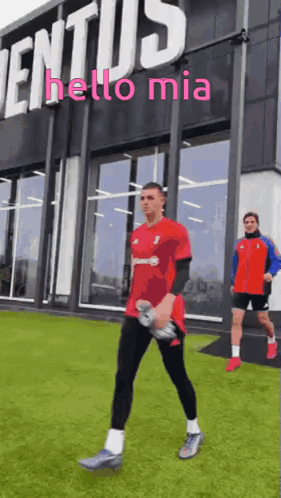 A Man In A Red Shirt Is Walking In Front Of A Building That Says " Hello Mia " GIF