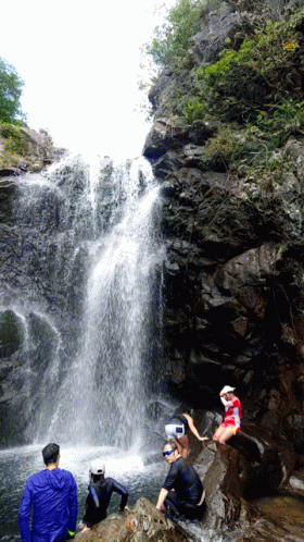 A Man In A Red Shirt Sits On A Rock Near A Waterfall GIF