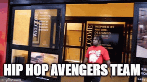 A Man In A Red Shirt Standing In Front Of A Building With The Words Hip Hop Avengers Team GIF