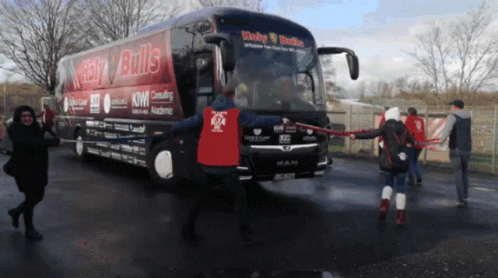 A Man In A Red Shirt Stands In Front Of A Bus That Says Lucky Bulls GIF