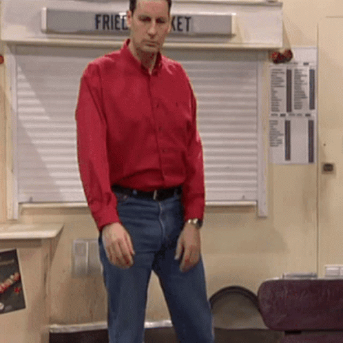A Man In A Red Shirt Stands In Front Of A Sign That Says Fried Bucket GIF