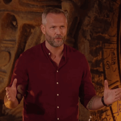 A Man In A Red Shirt Stands In Front Of A Wall With The Word Survivor On It GIF