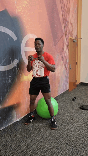 A Man In A Red Shirt Stands On A Green Ball GIF