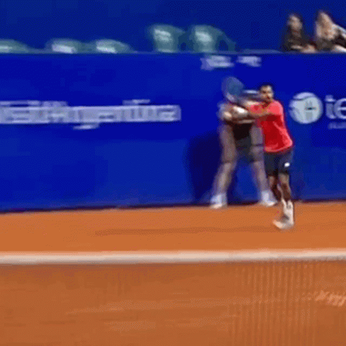 A Man In A Red Shirt Swings A Tennis Racquet On A Tennis Court GIF