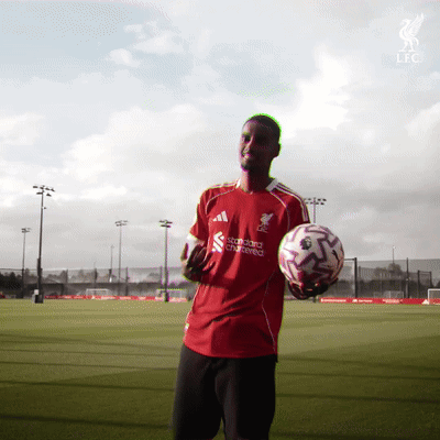 A Man In A Red Shirt That Says Standard Chartered On It Holds A Soccer Ball GIF