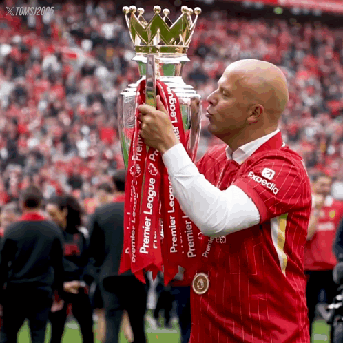A Man In A Red Shirt With Expedia On It Kisses The Trophy GIF
