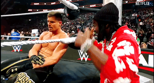 a man in a red shirt with the letter a on it is talking to another man in a wrestling ring