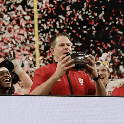 A Man In A Red Shirt With The Letter U On It Holds A Football GIF