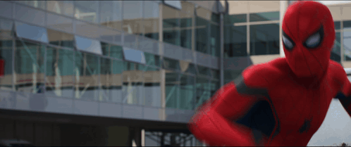 A Man In A Red Spiderman Suit Is Standing In Front Of A Building GIF