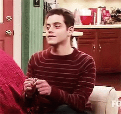 A Man In A Red Striped Sweater Is Sitting On A Couch Holding A Knitting Needles . GIF