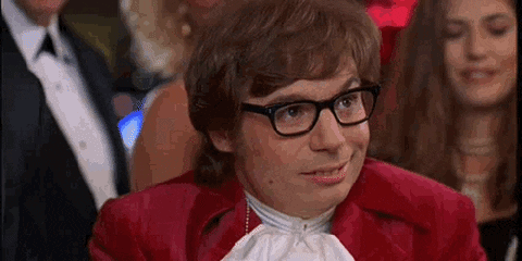 A Man In A Red Suit And Glasses Is Sitting In A Crowd . GIF