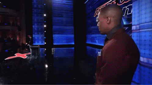 A Man In A Red Suit And Tie Stands In Front Of A Sign That Says America 'S Got Talent GIF