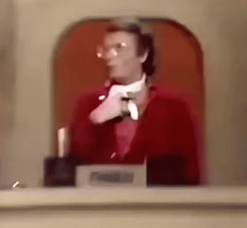 A Man In A Red Suit And White Tie Is Standing In Front Of A Glass Door . GIF