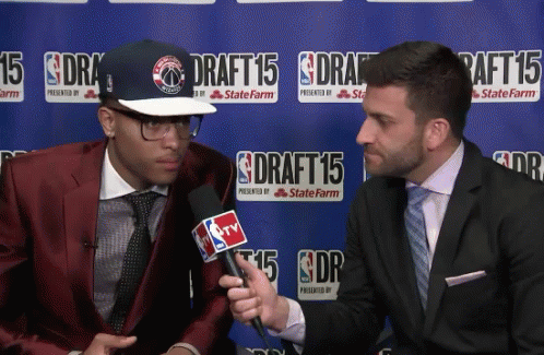 a man in a red suit is being interviewed by a man in a suit in front of a sign that says draft 15