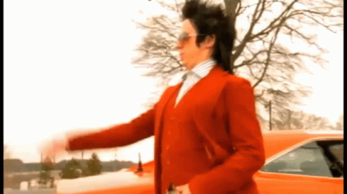 A Man In A Red Suit Is Standing In Front Of A Red Car GIF