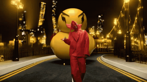 A Man In A Red Suit Stands In Front Of A Large Yellow Ball GIF