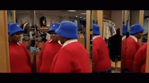 A Man In A Red Sweater And Blue Hat Looks At Himself In The Mirror GIF