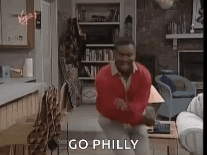 A Man In A Red Sweater Is Dancing In A Living Room With The Words `` Go Philly '' Written On The Screen . GIF
