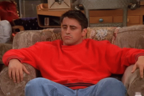 A Man In A Red Sweater Is Sitting On A Couch With The Words Ah-Ha Written On His Chest . GIF