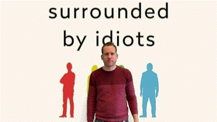 A Man In A Red Sweater Is Standing In Front Of A Sign That Says Surrounded By Idiots GIF