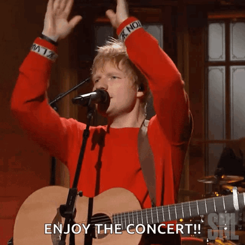 A Man In A Red Sweater Singing Into A Microphone With The Words Enjoy The Concert GIF