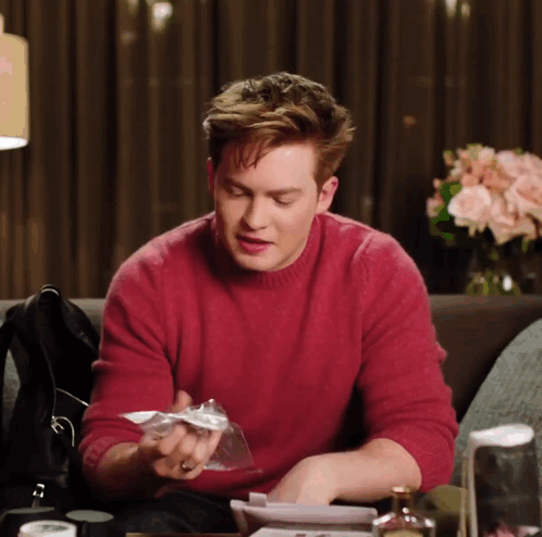 A Man In A Red Sweater Sits At A Table GIF
