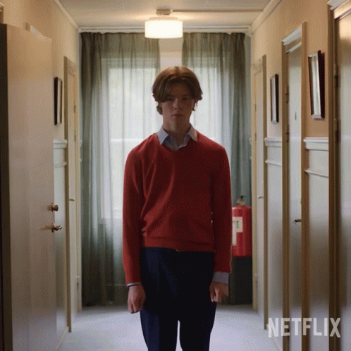A Man In A Red Sweater Stands In A Hallway With Netflix Written On The Wall Behind Him GIF