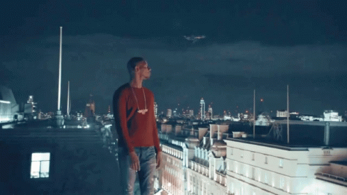 A Man In A Red Sweater Stands On The Roof Of A Building GIF