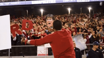 a man in a red sweatshirt stands in front of a crowd holding a sign that says " cal top passer "