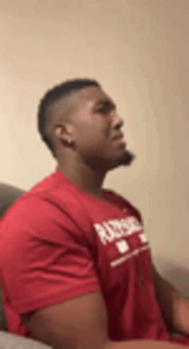 A Man In A Red T-Shirt Is Sitting On A Couch . GIF