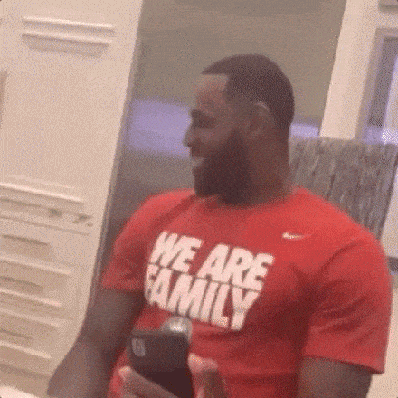 a man in a red t-shirt that says `` we are family '' is holding a cell phone .