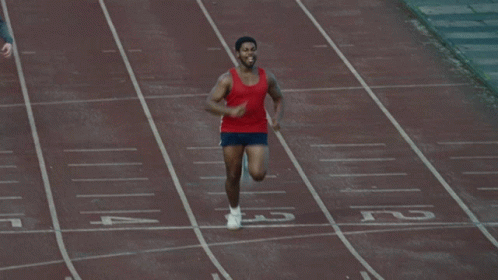 A Man In A Red Tank Top Is Running On A Track With His Arms Outstretched GIF