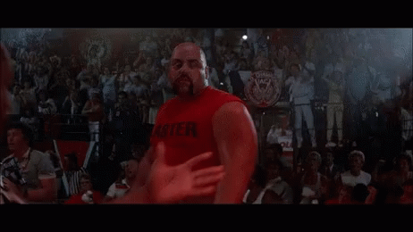 A Man In A Red Tank Top Is Standing Next To Another Man In A Wrestling Ring . GIF