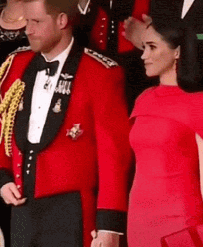 A Man In A Red Tuxedo And A Woman In A Red Dress Are Standing Next To Each Other And Holding Hands . GIF