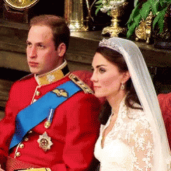 A Man In A Red Uniform Sits Next To A Woman In A White Dress And Veil GIF