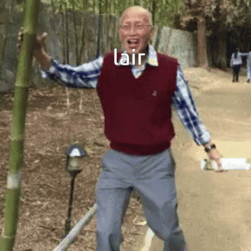 A Man In A Red Vest Is Holding A Bamboo Pole With The Word Lair Above Him GIF