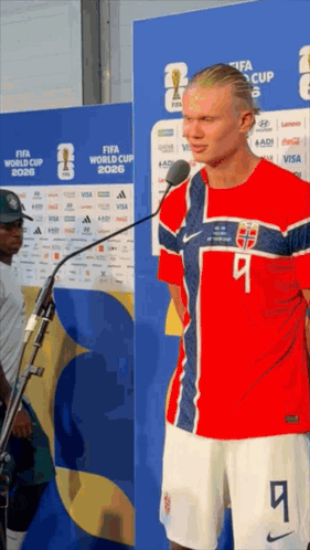 A Man In A Red White And Blue Jersey With The Number 9 On It Stands In Front Of A Microphone GIF