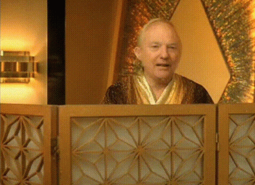 A Man In A Robe Is Behind A Wooden Screen And Smiling GIF