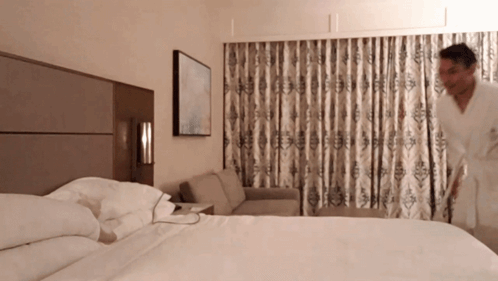 A Man In A Robe Is Standing In A Hotel Room GIF