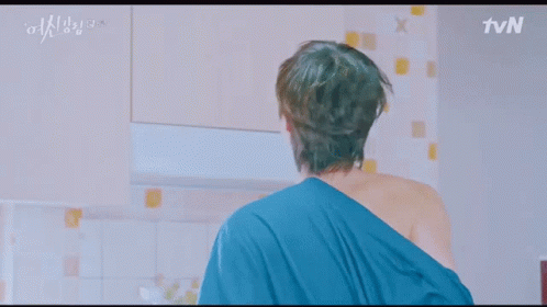 A Man In A Robe Is Standing In A Kitchen With A Microwave And A Refrigerator . GIF