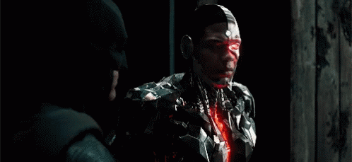 A Man In A Robotic Suit Is Standing Next To A Man In A Batman Hat . GIF