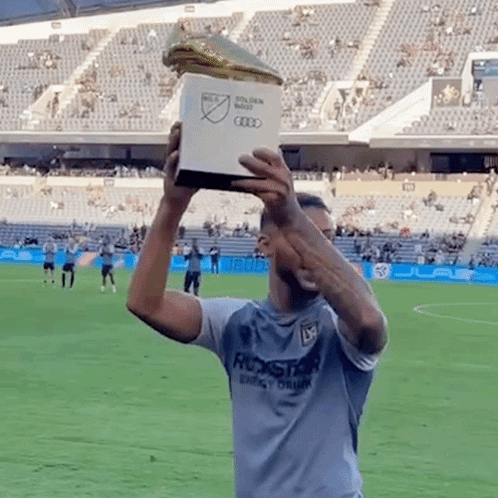 a man in a rockstar energy drink shirt holds up a trophy on a soccer field