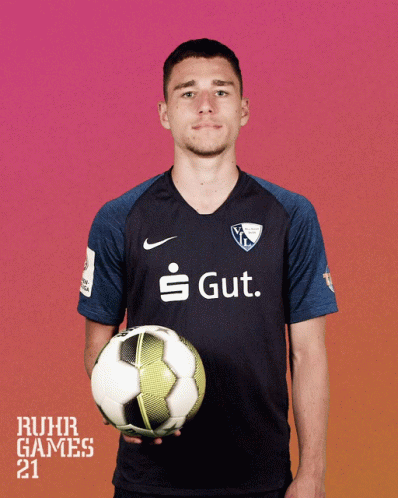 a man in a ruhr games shirt holds a soccer ball in his hands